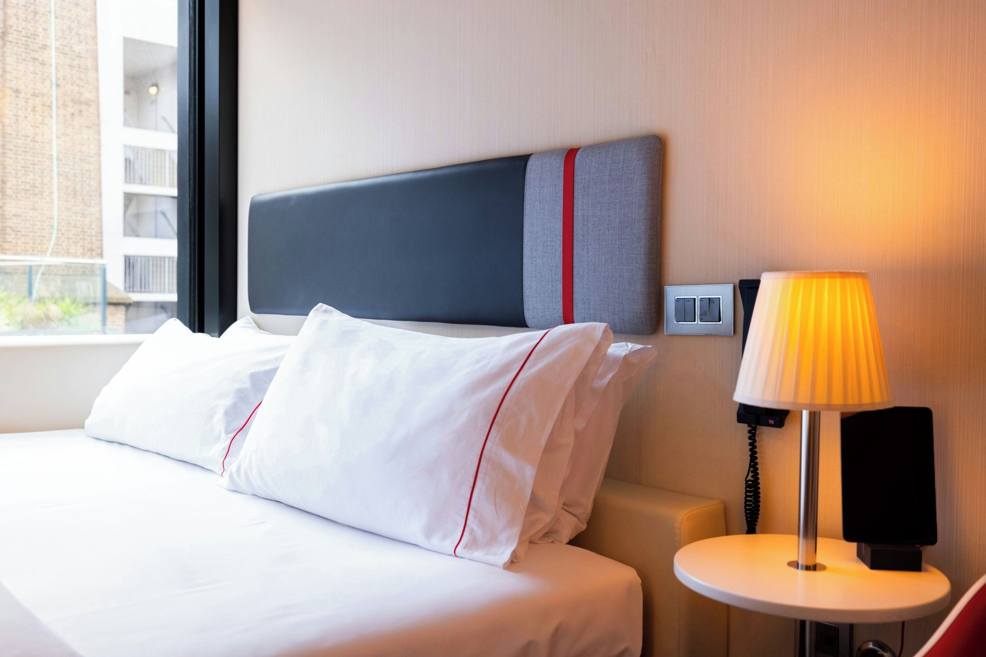 Een hotelkamer met een bed, nachtkastje met lamp en een telefoon aan de muur.