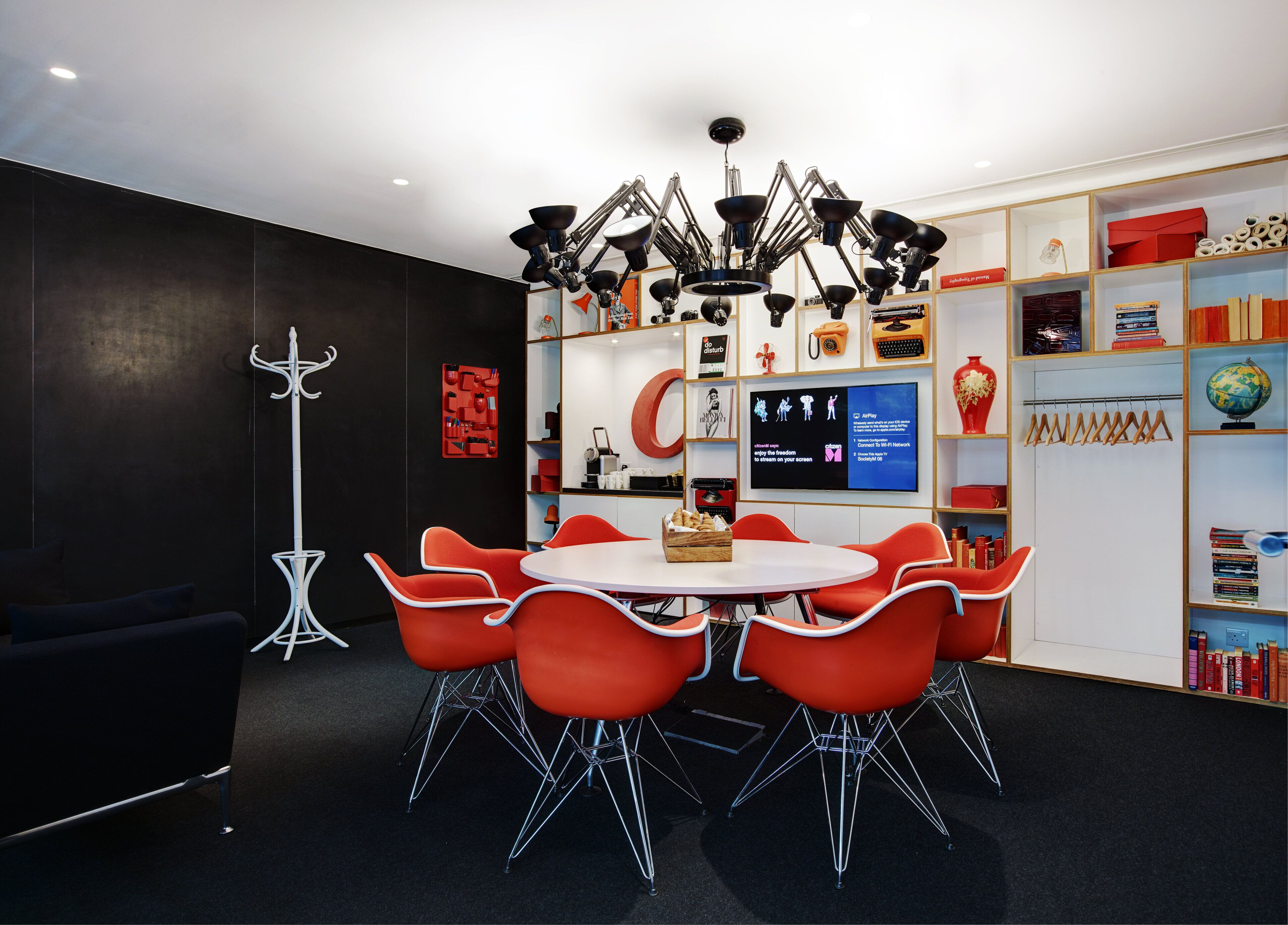 Une salle de conférence moderne, dotée d’une table ronde, de chaises rouges et d’un luminaire fixé au plafond.