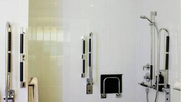 A modern bathroom with white tiled walls, a black floor, and a shower area with a handheld showerhead and a handheld shower attachment.