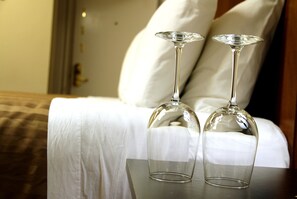 Two empty wine glasses on a table in a hotel room with a bed and pillows in the background.