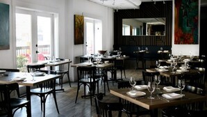 En restaurant med flere borde og stole, store vinduer og kunst på væggene.