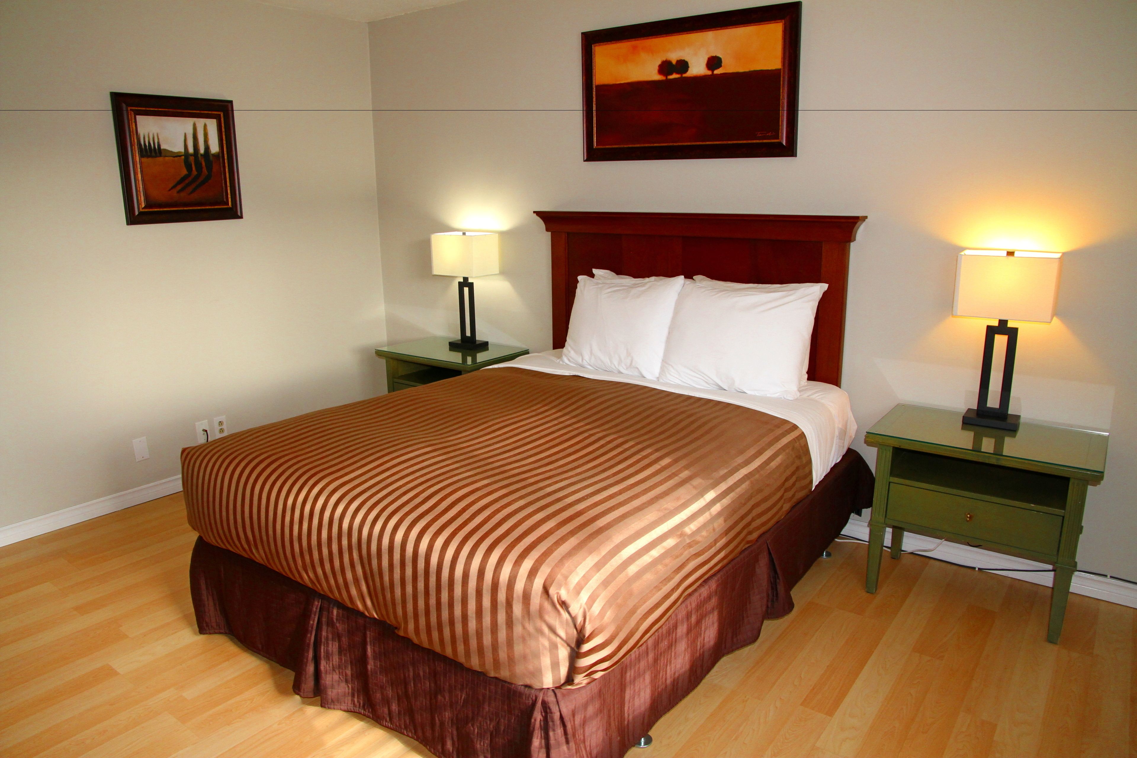 Habitación de hotel con una cama grande, dos mesitas de noche con lámparas, un cuadro enmarcado en la pared y suelo de madera.