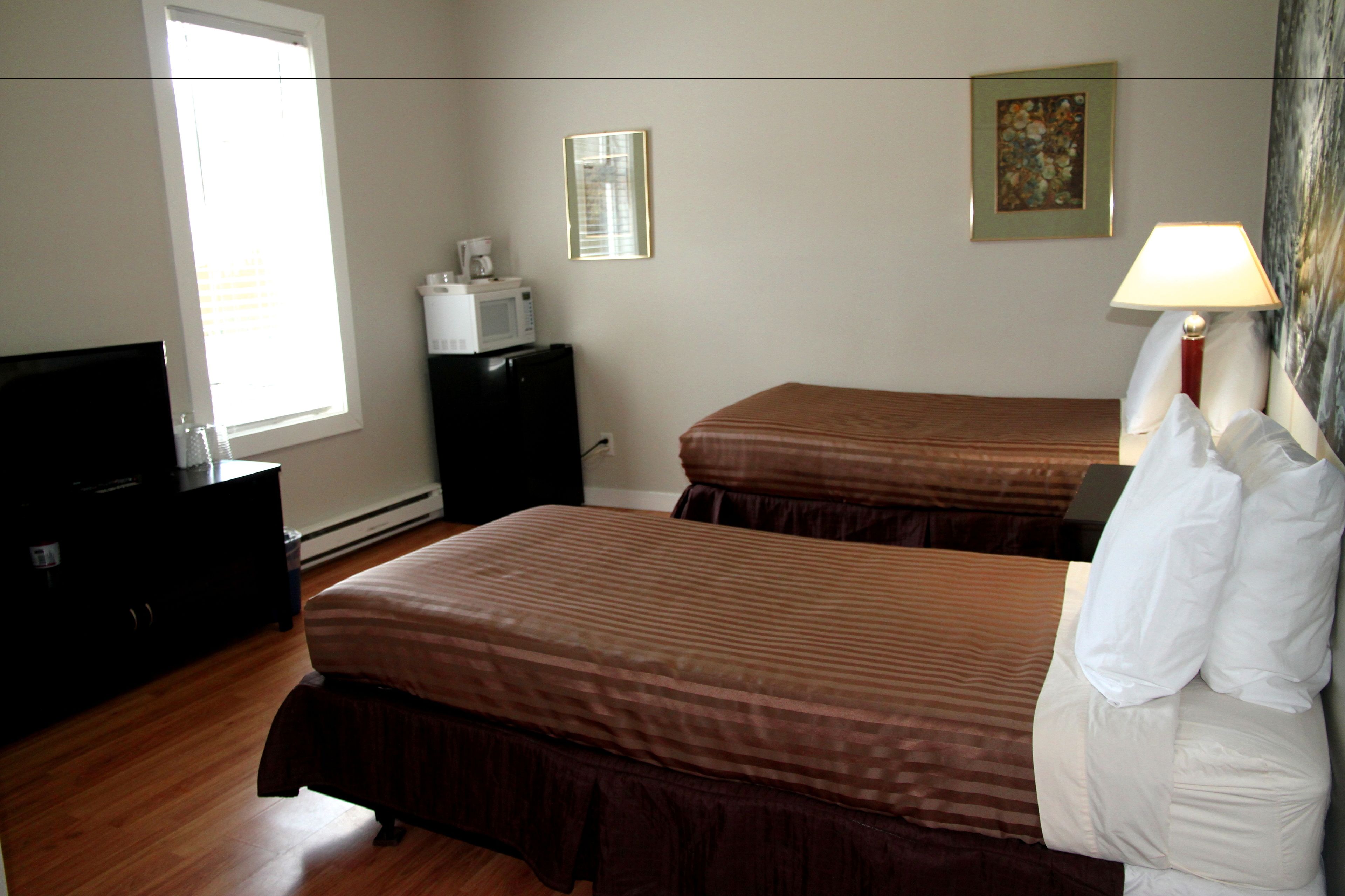 A hotel room with two beds, a dresser, a microwave, and a lamp.