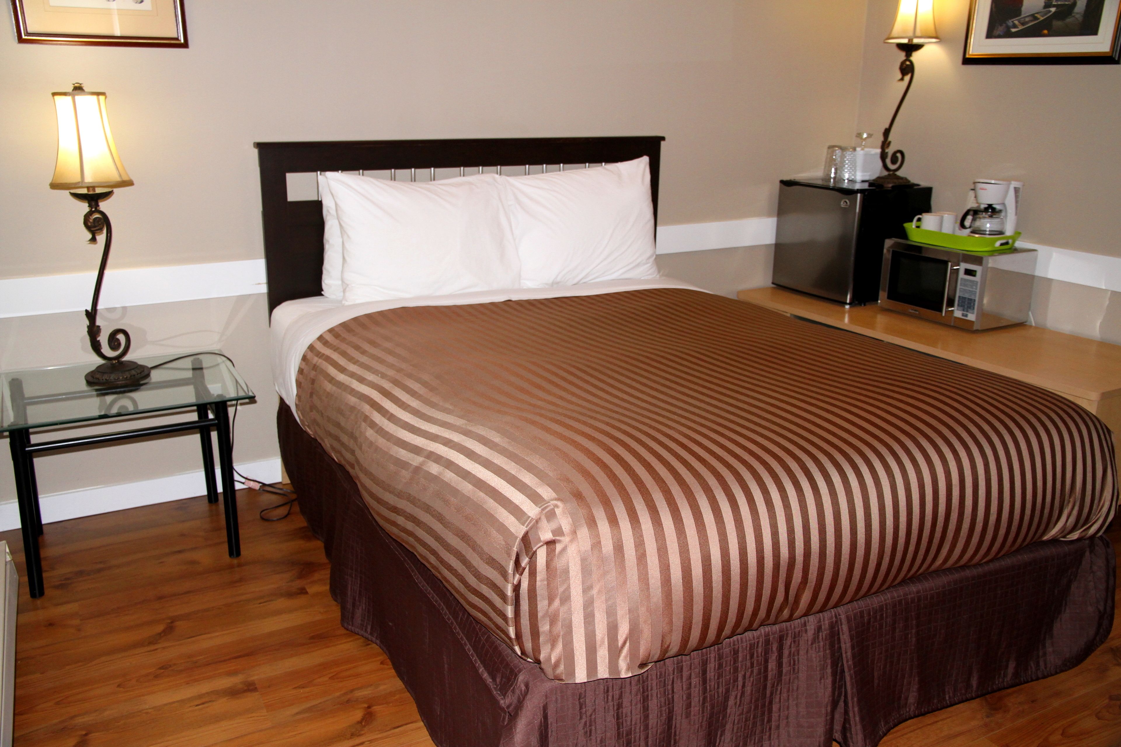 A neatly made bed with a striped bedspread, a bedside table with a lamp, and a small refrigerator with a coffee maker on top.