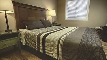Una cama bien hecha con una colcha a rayas, dos lámparas de noche, un cabecero de madera y una ventana con persianas.