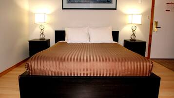 A neatly made bed with a brown bedspread, two bedside tables with lamps, a framed picture on the wall, and a door with an emergency exit sign.