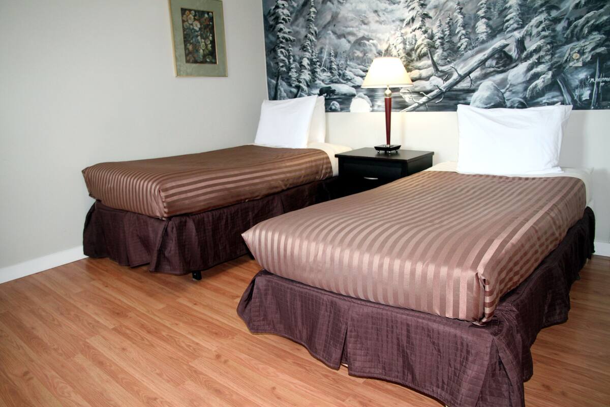 Hotellihuone, jossa on kaksi sänkyä, yöpöytä lampun kanssa ja taulu seinällä.
