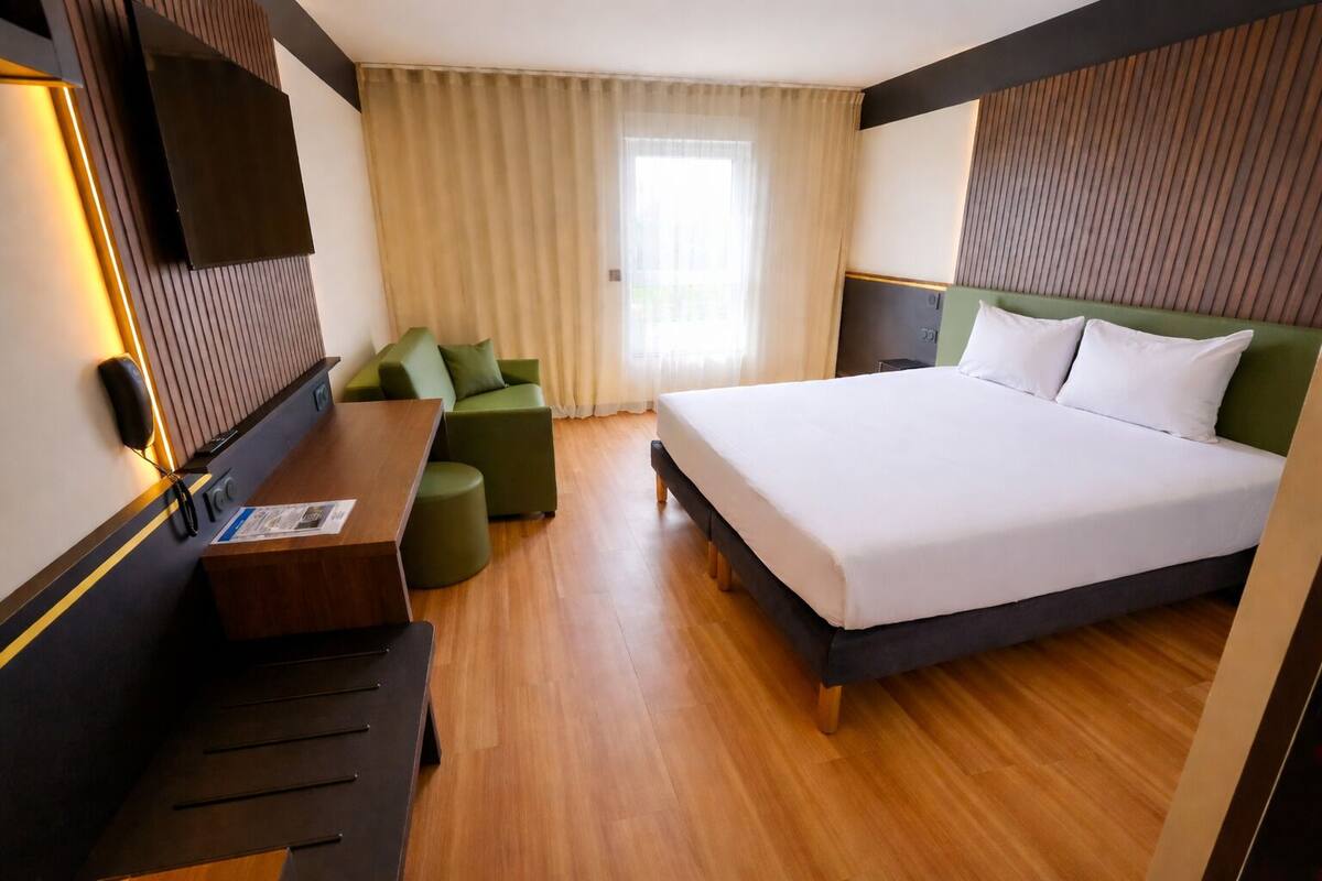Una habitación de hotel con cama, escritorio, teléfono, sofá y ventana con cortinas.
