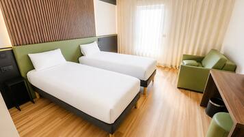 Habitación de hotel con dos camas individuales, un sofá verde, una mesita pequeña y suelo de madera.