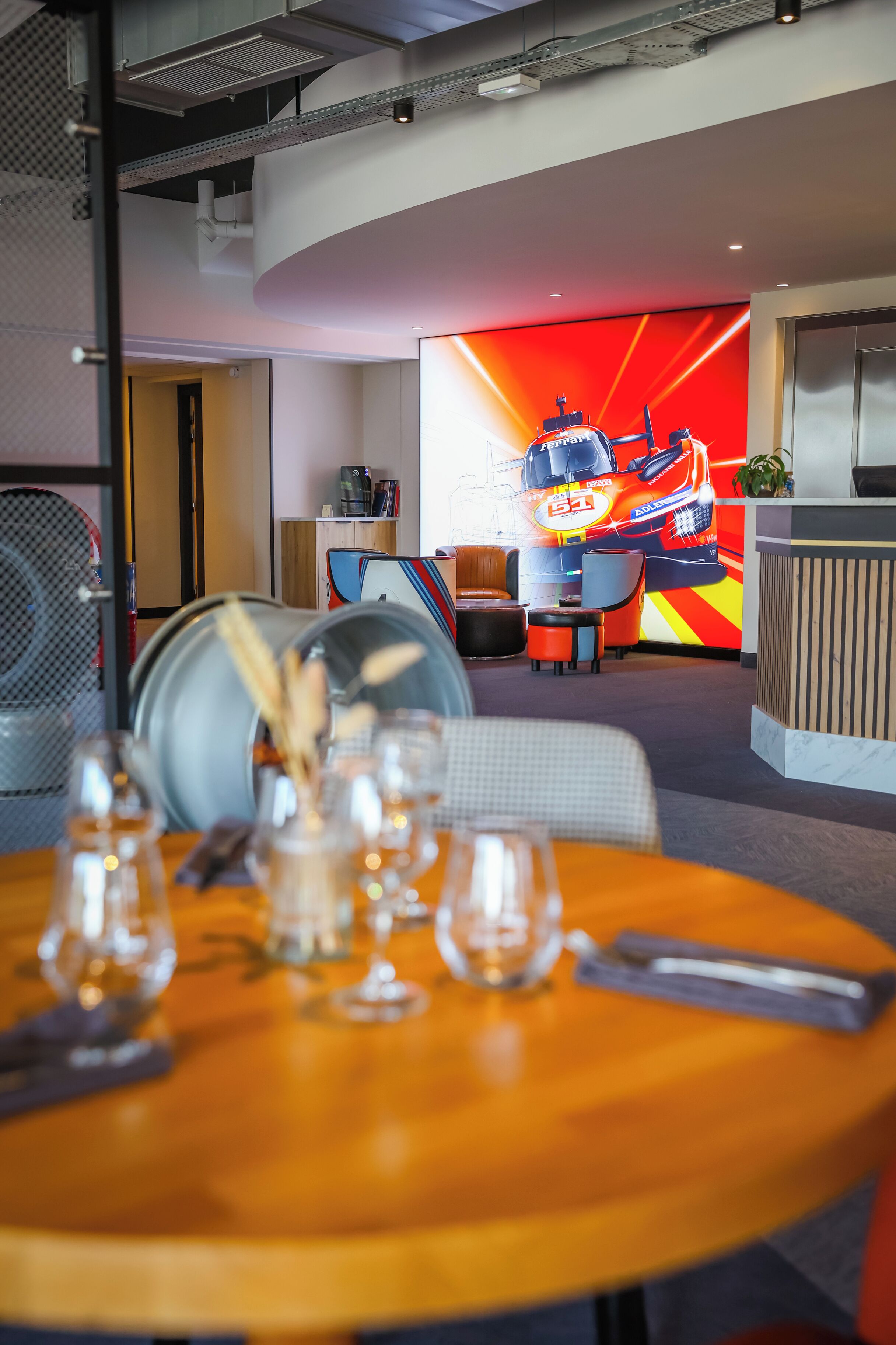 A modern hotel lobby with a reception desk, seating area, and a large digital screen displaying a racing theme.