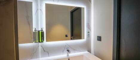 Un baño con lavabo blanco, espejo y pared de mármol.