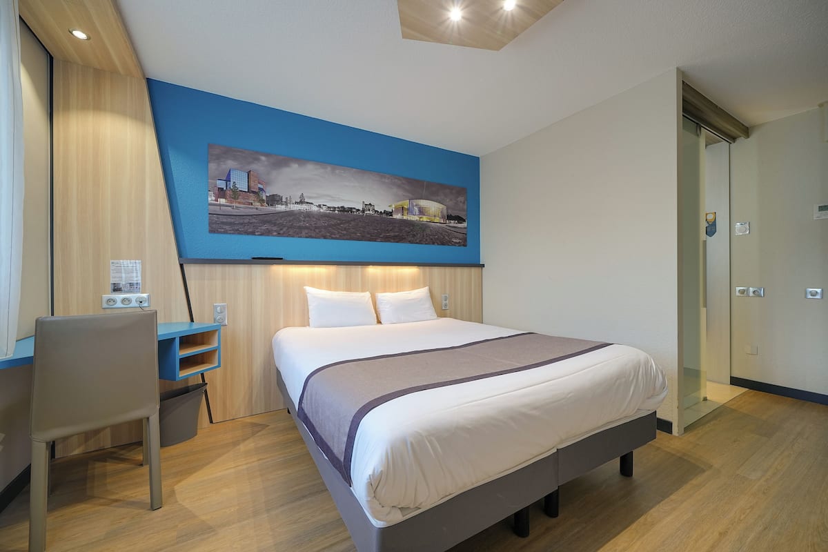 Habitación de hotel con una cama, un escritorio y una silla. Hay un cuadro en la pared sobre la cama.