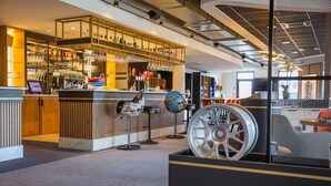 A modern bar area with a counter, bar stools, and a large decorative wheel. - Brit Hotel Le Cottage (Arnage)