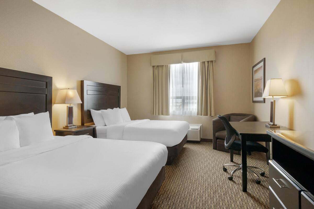 A hotel room with two beds, a desk, a chair, a TV, and a window with curtains.