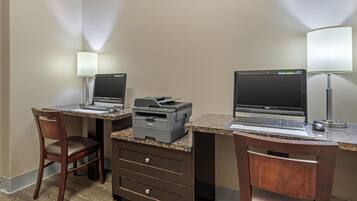 Een hotelkamer met twee bureaus, elk met een laptop en een printer, een stoel en een bureaulamp.
