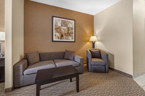 Ein Hotelzimmer mit grauem Sofa, einem kleinen Sessel, einem dunklen Couchtisch und einer Lampe.
