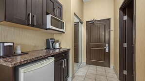 A compact kitchen with dark wooden cabinets, a built-in microwave, a coffee maker, and a dishwasher. - Best Western Estevan Inn & Suites (Estevan)