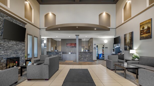 A spacious lobby with grey sofas, a flat-screen TV, a stone fireplace, and a central island with a kitchen area. - Best Western Estevan Inn & Suites (Estevan)