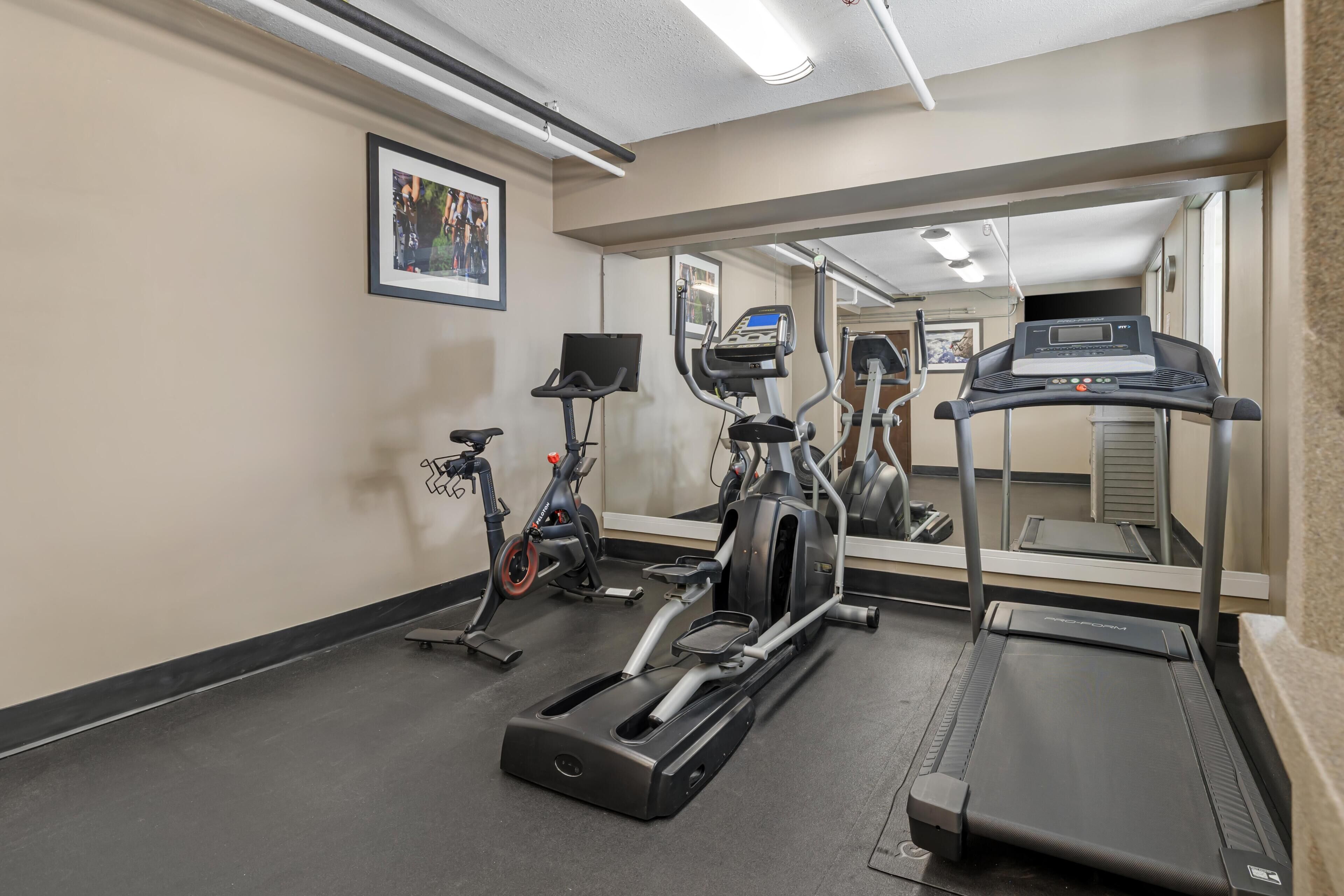 Un gimnasio con cintas de correr, bicicletas estáticas y un espejo grande.