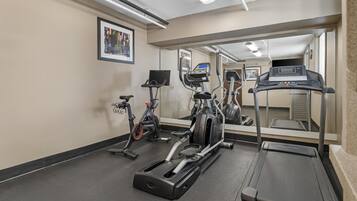 Un gimnasio con cintas de correr, bicicletas estáticas y un espejo grande.