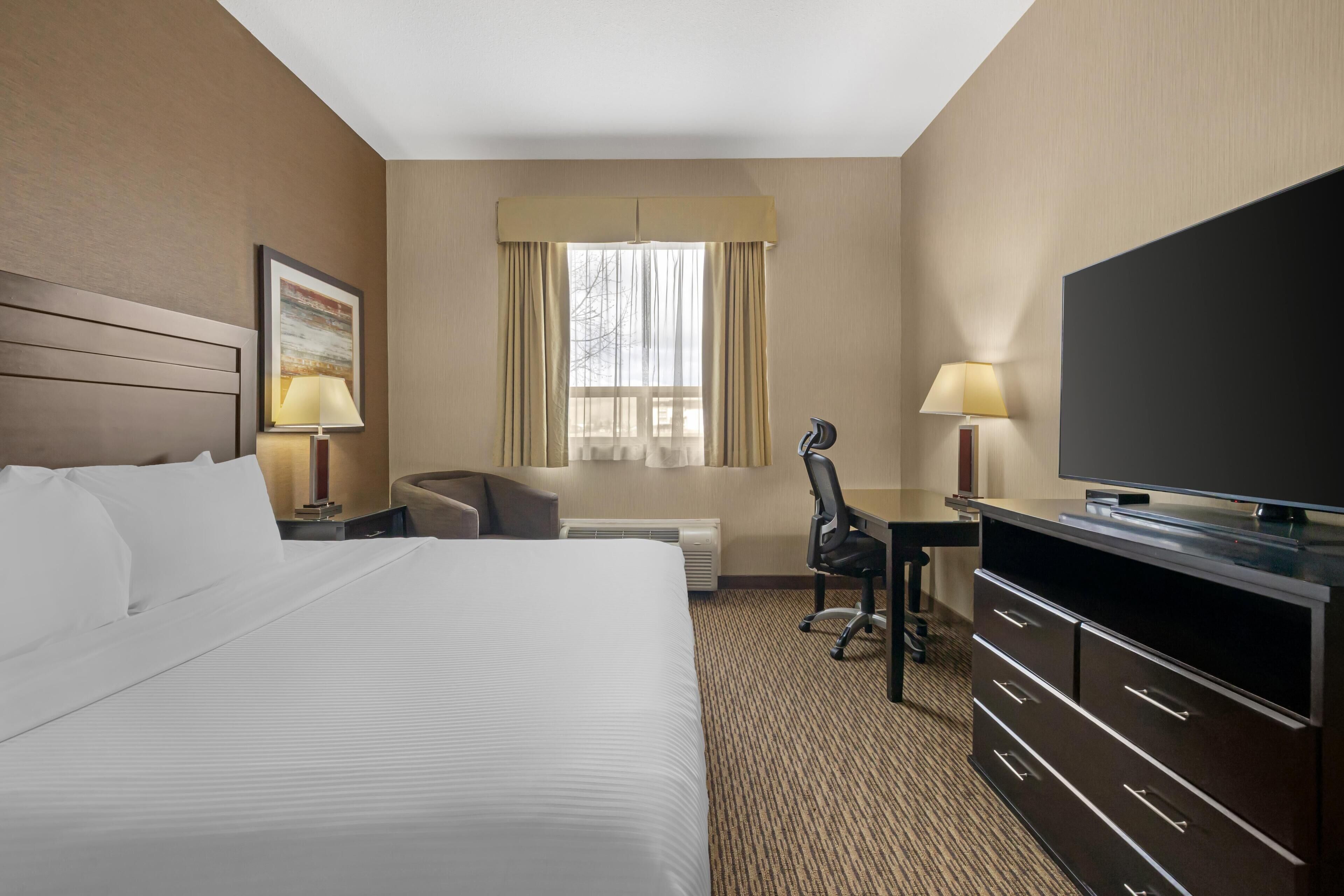 A hotel room with a large bed, a desk with a chair, a television, and a window with curtains.