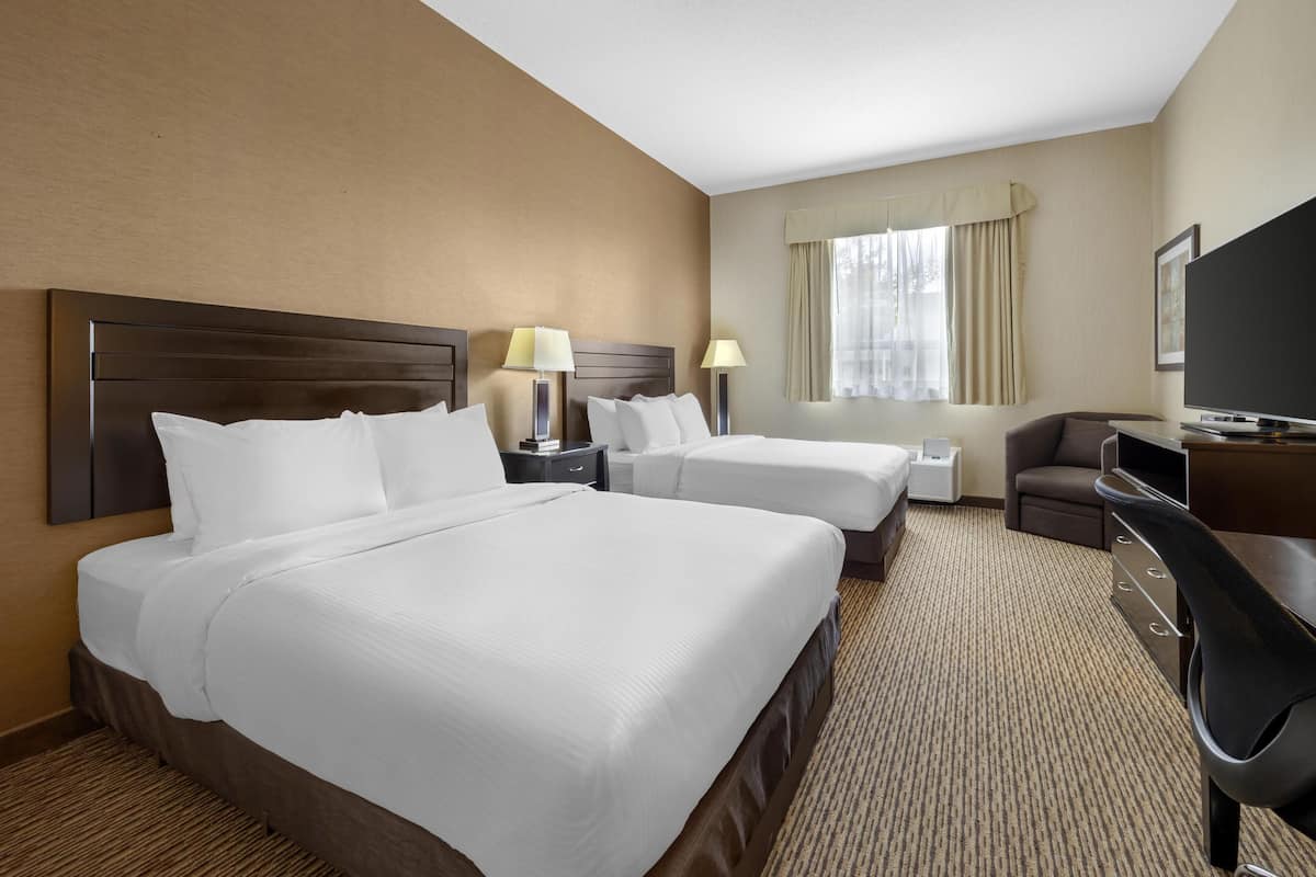 A hotel room with two beds, a desk, a chair, a television, and a window with curtains.