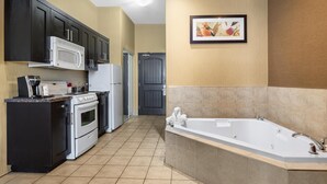 A compact kitchen with a microwave, stove, and refrigerator, a bathroom with a bathtub, and a door leading to another room. - Best Western Estevan Inn & Suites (Estevan)