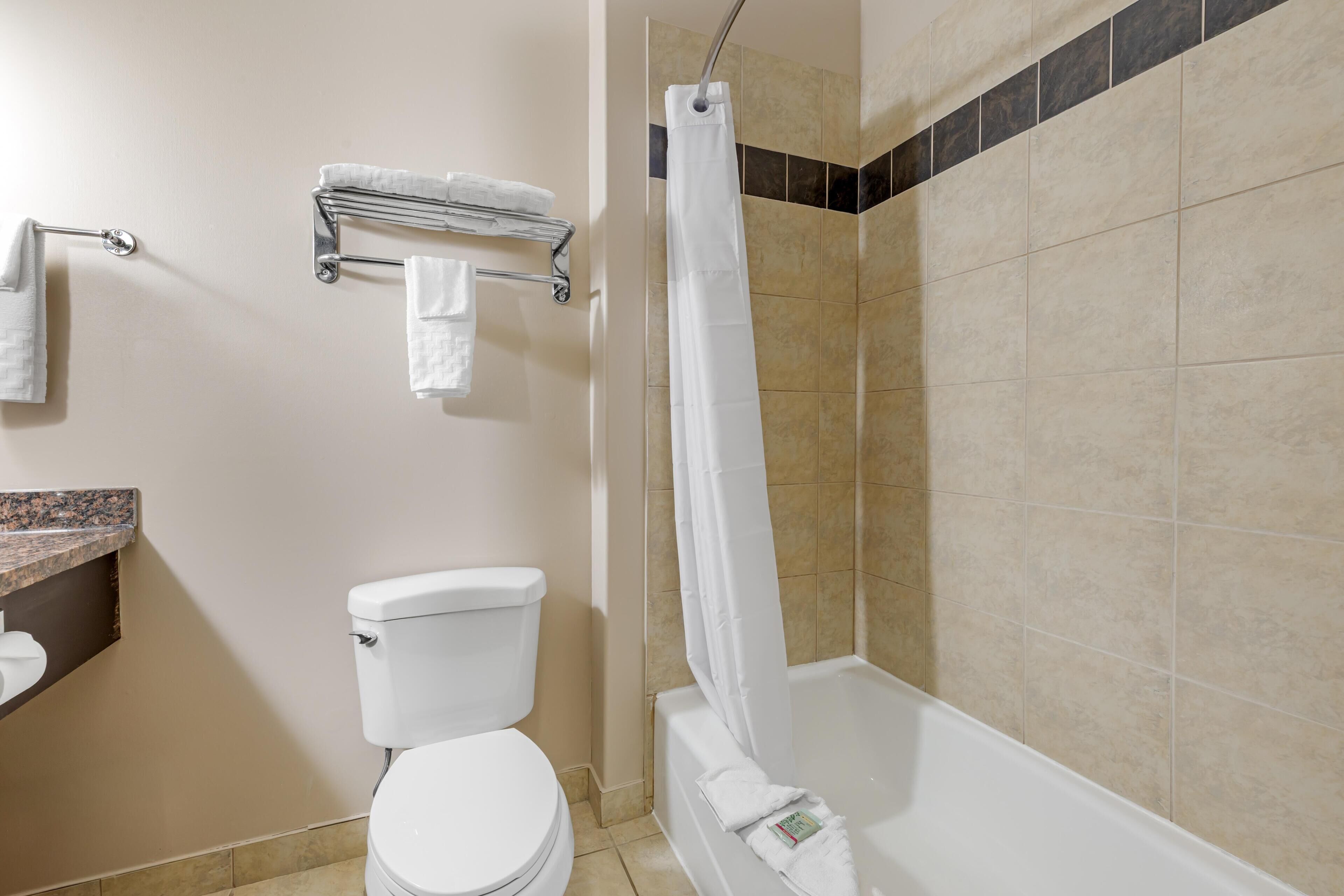 A bathroom with a toilet, a shower with a curtain, a towel rack, and a marble countertop.