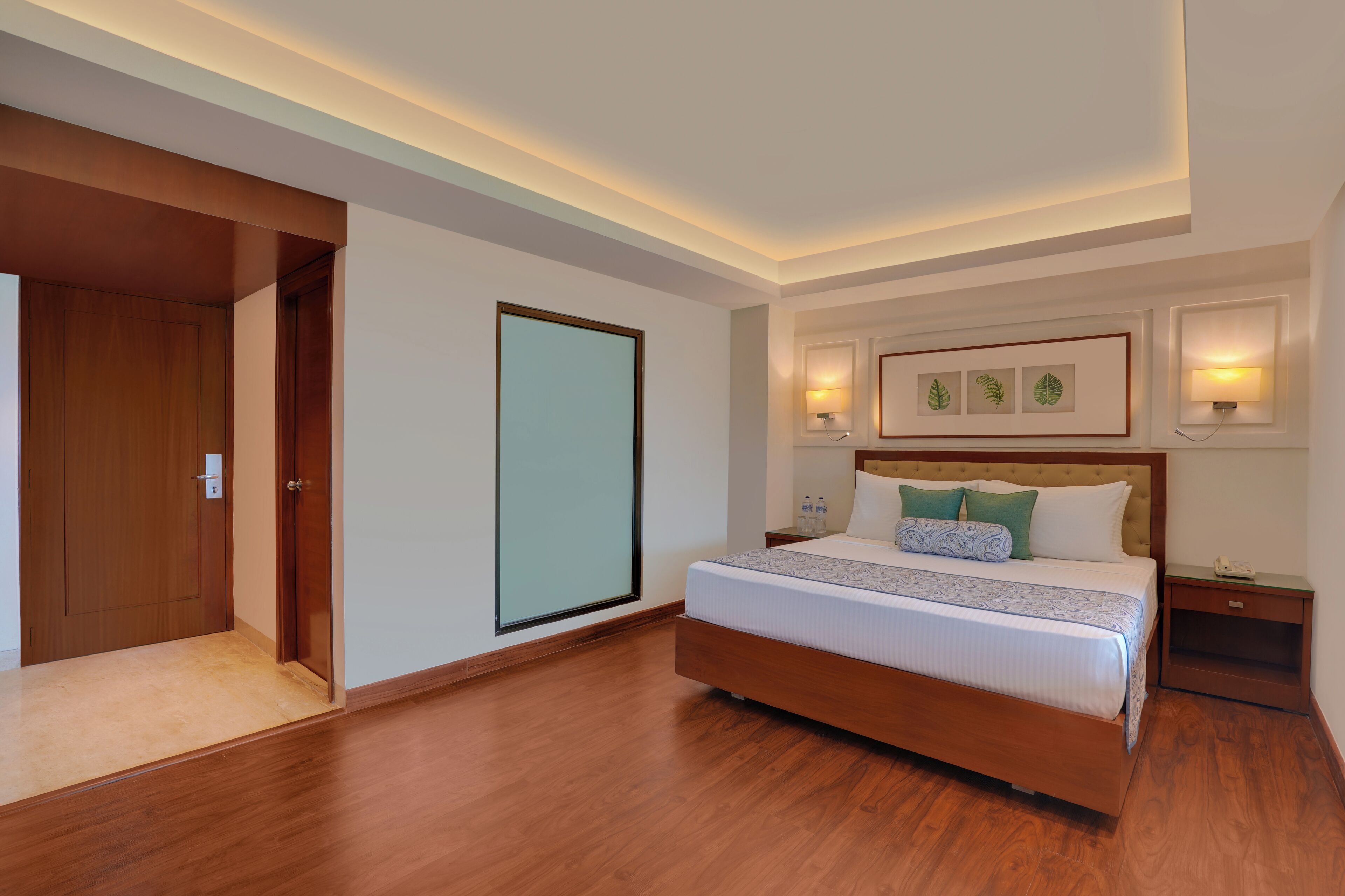 A modern hotel room with a wooden floor, a large bed with a headboard, bedside tables, and framed artwork on the wall.