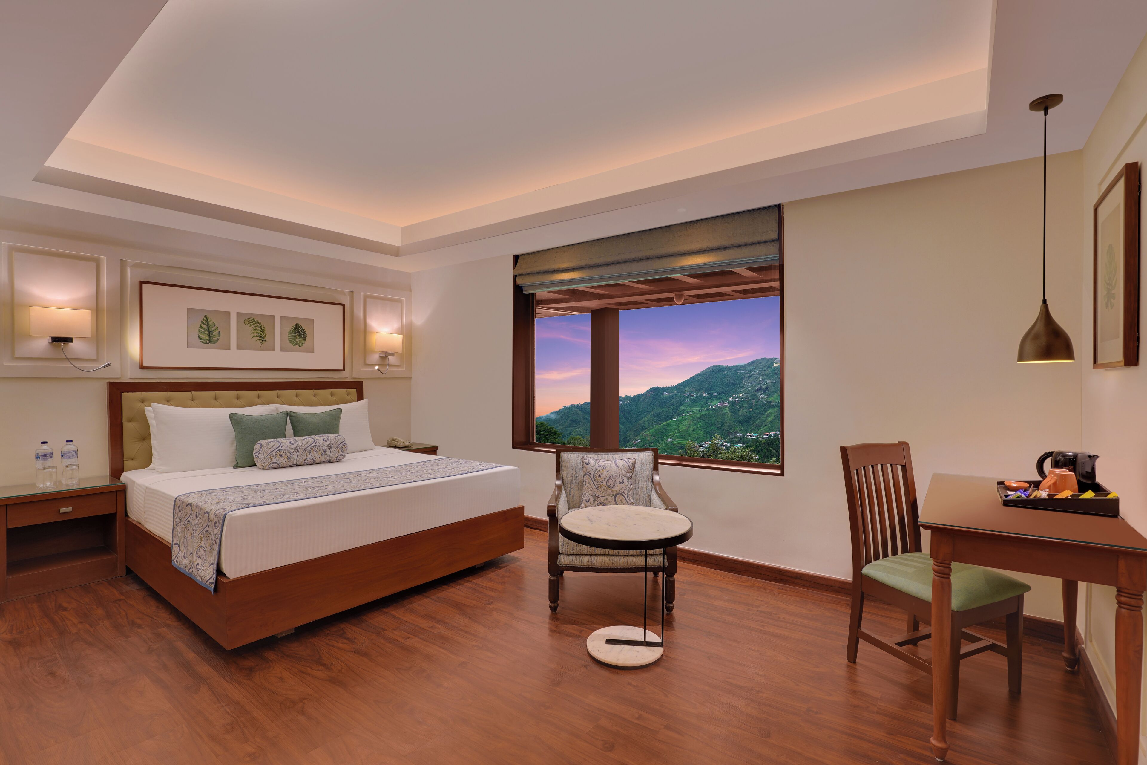 A bedroom with a bed, a chair, a table, and a window with a view of mountains.