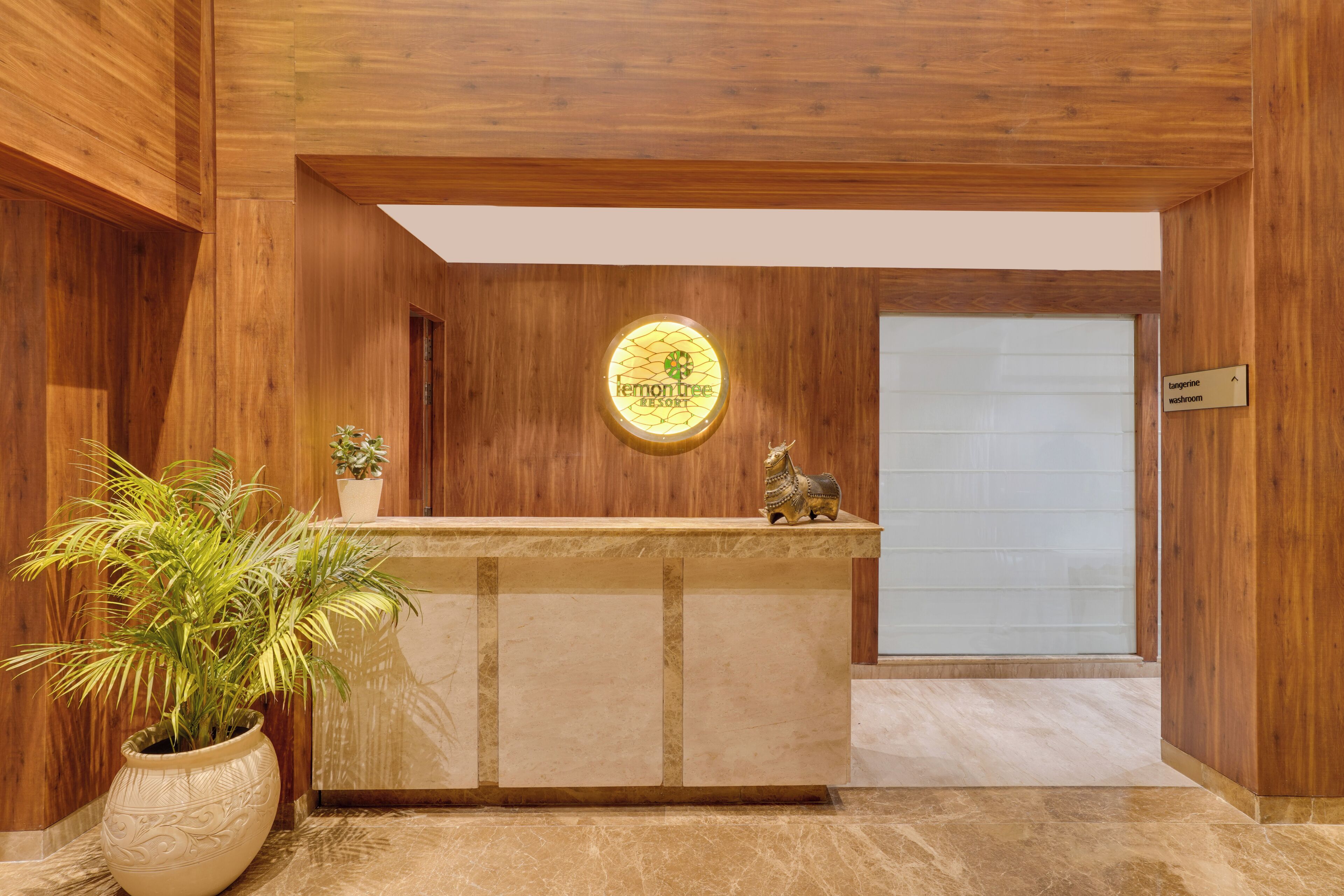 Un mostrador de recepción con detalles de madera, una planta en maceta y un letrero que indica un baño con aroma a mandarina.