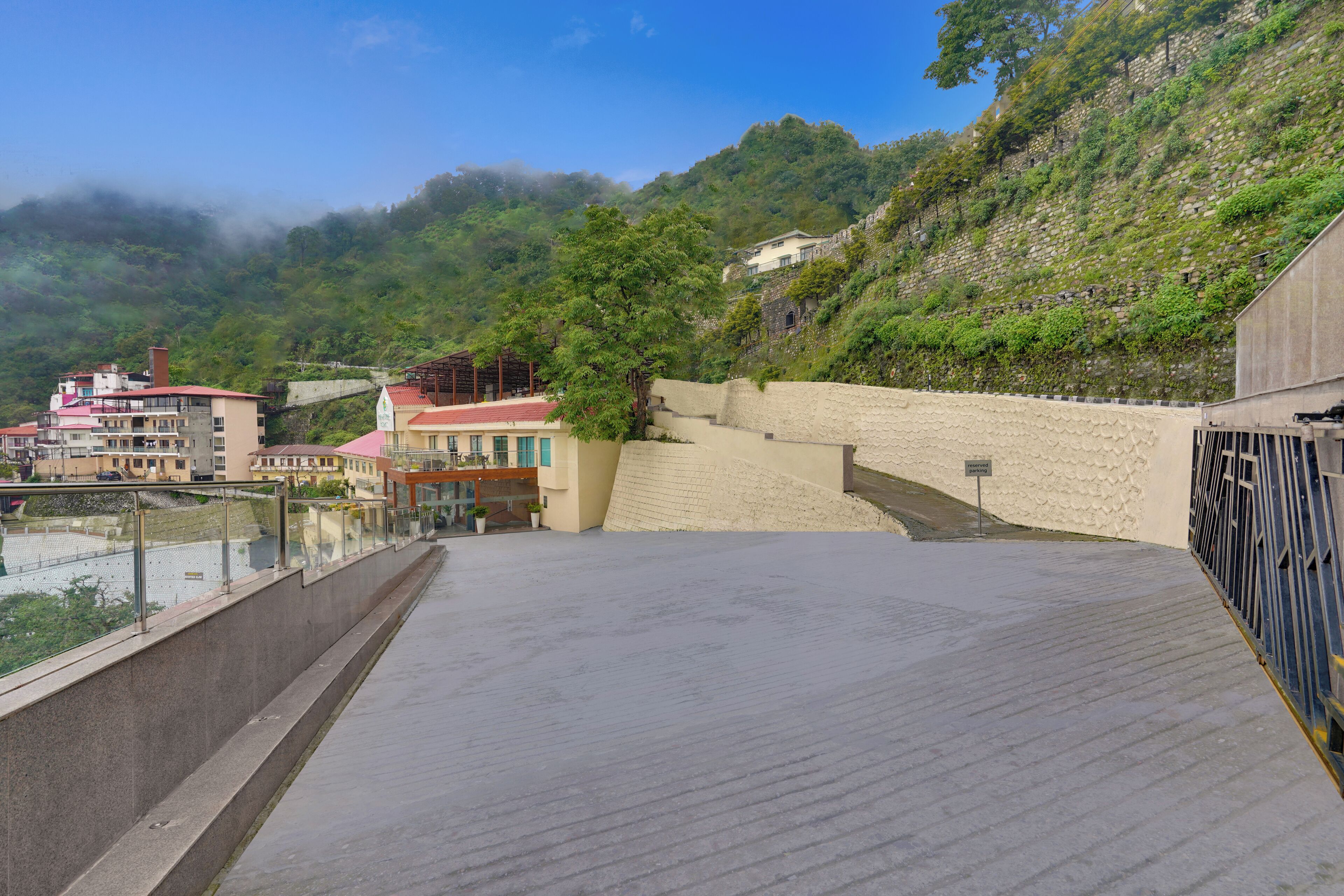 A rooftop terrace with a view of a hillside, a stone wall, and buildings in the background.