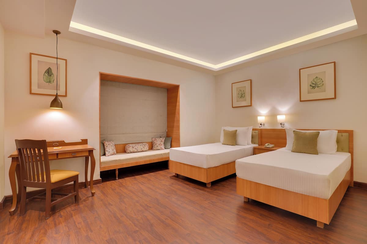 A hotel room with two beds, a desk, a chair, and a sofa.