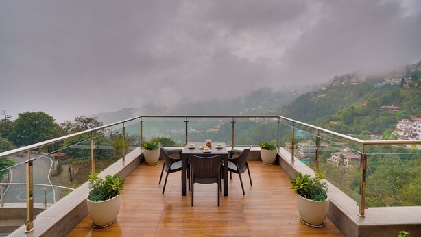 A terrace with a table and chairs, potted plants, and a view of a hilly landscape. - Lemon Tree Resort, Mussoorie (Dehradun)