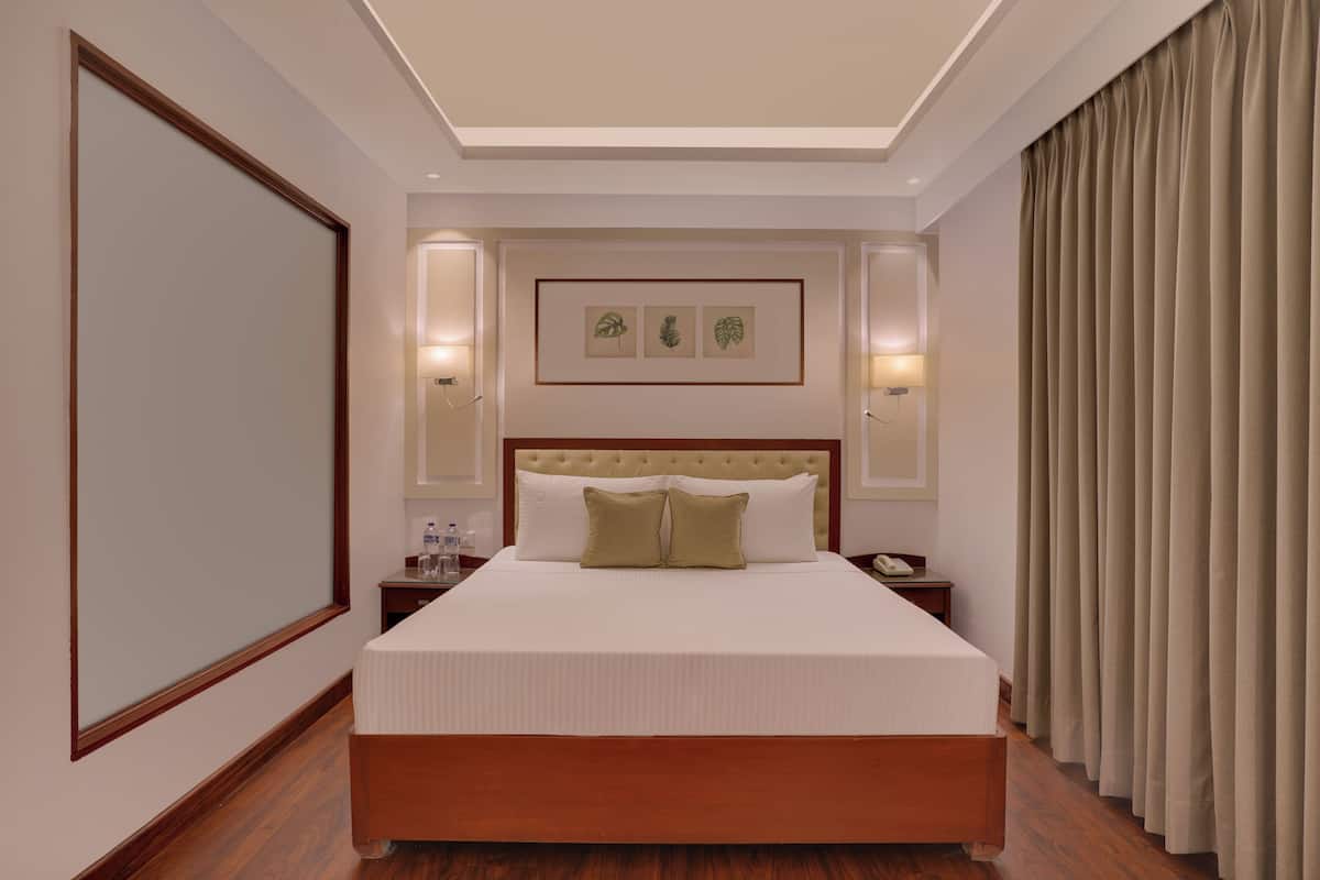 A hotel room with a large bed, wooden headboard, two bedside tables, a nightstand, and a framed picture on the wall.