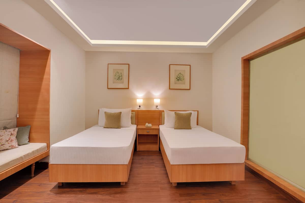 A hotel room with two single beds, a wooden nightstand, a small table, and a sofa.