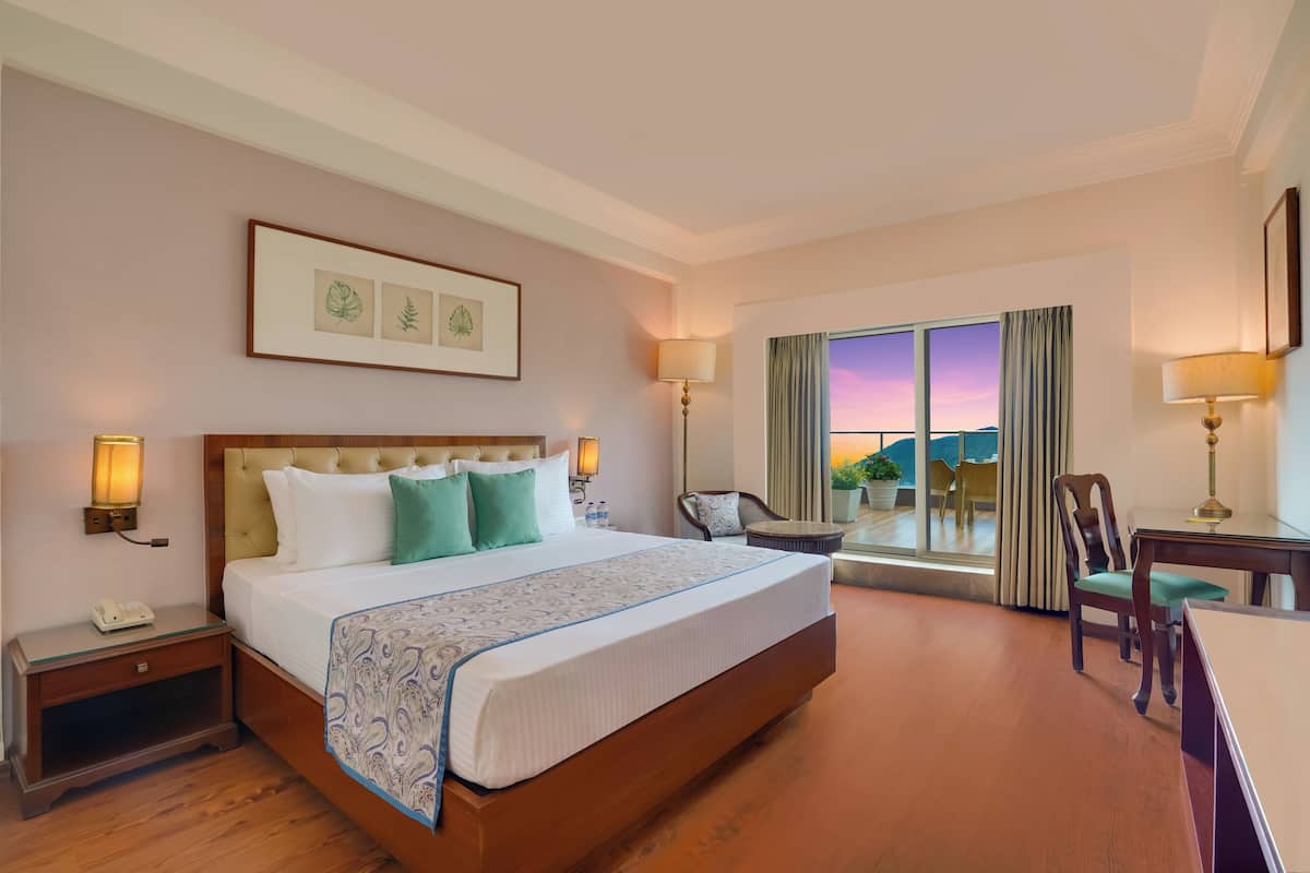 A hotel room with a large bed, bedside lamps, a desk, and a view of the sunset through the window.