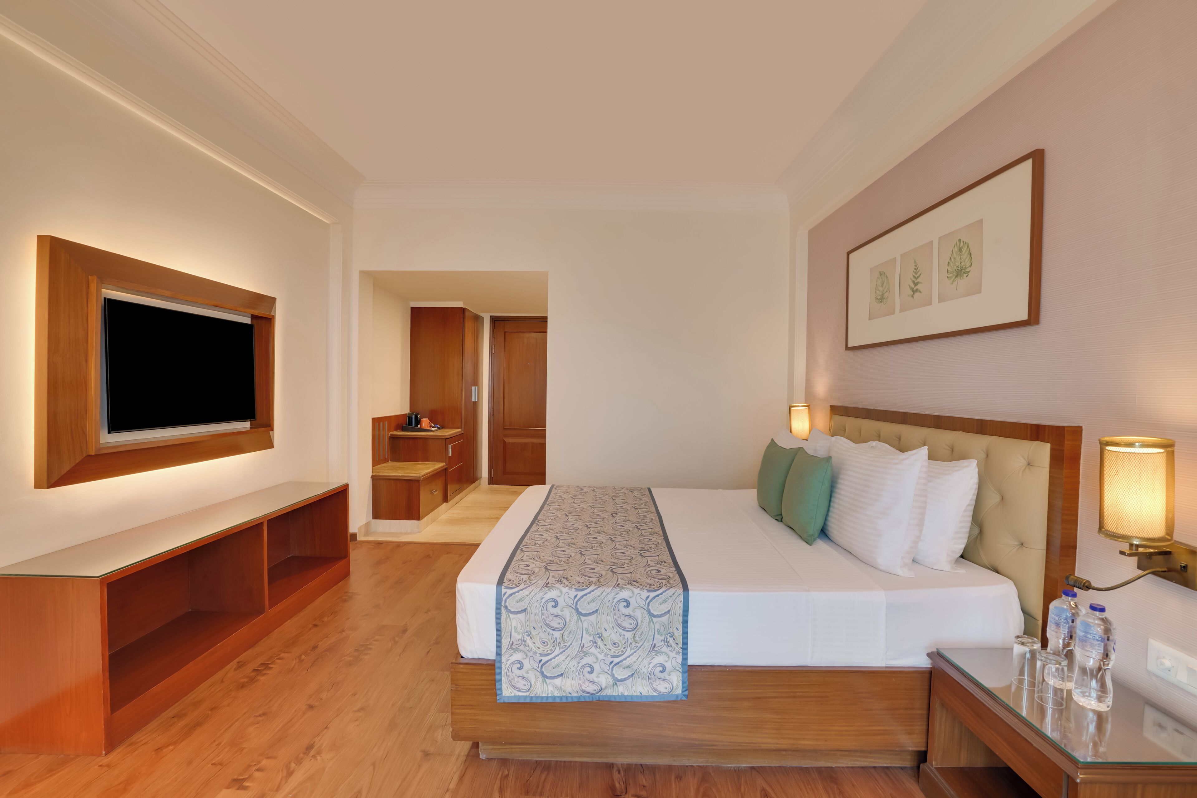 A hotel room with a large bed, a TV mounted on the wall, a bedside table, and a framed picture above the bed.