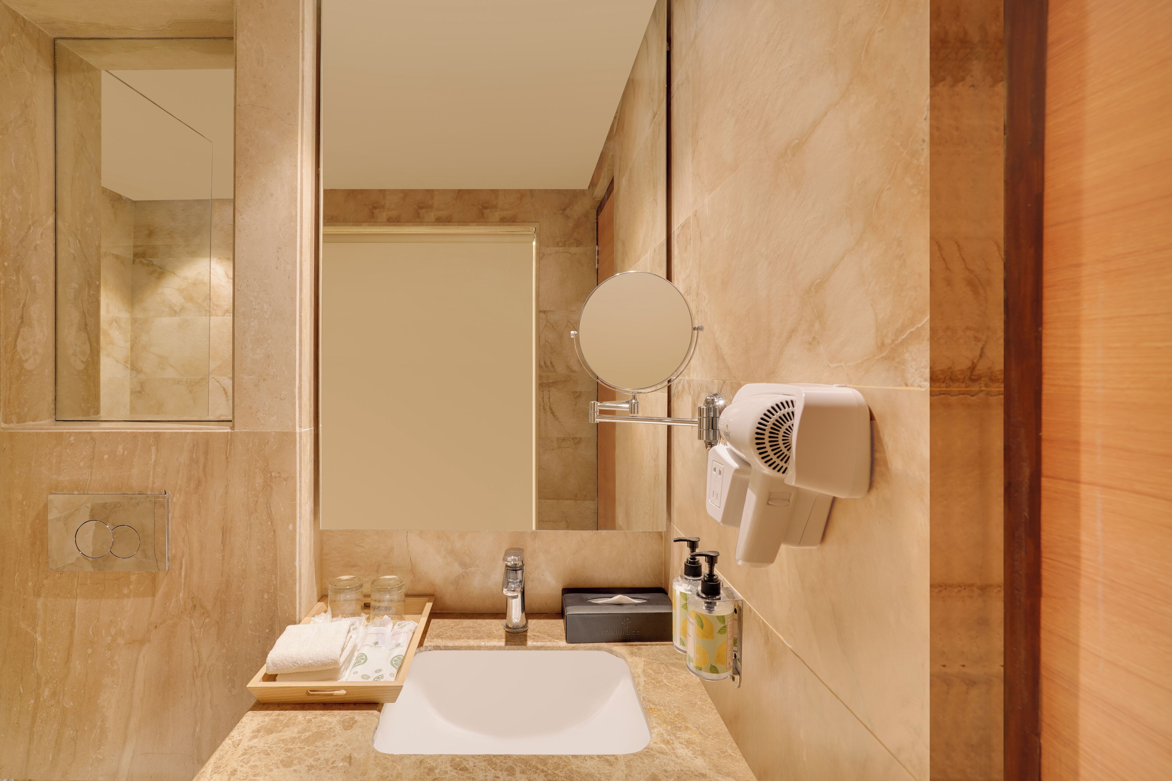 Ein modernes Badezimmer mit Marmorwaschtisch, rundem Spiegel, Föhn und Handtuchhalter.