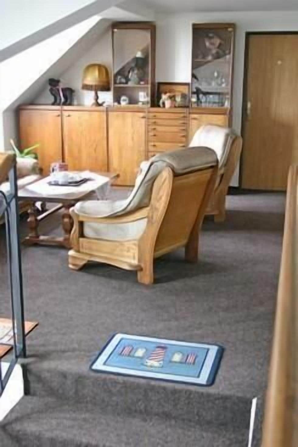 A room with a wooden cabinet, a chair, a small table, and a carpeted floor.