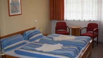 Een hotelkamer met een groot bed, twee rode stoelen, een kleine tafel en een raam met gordijnen.