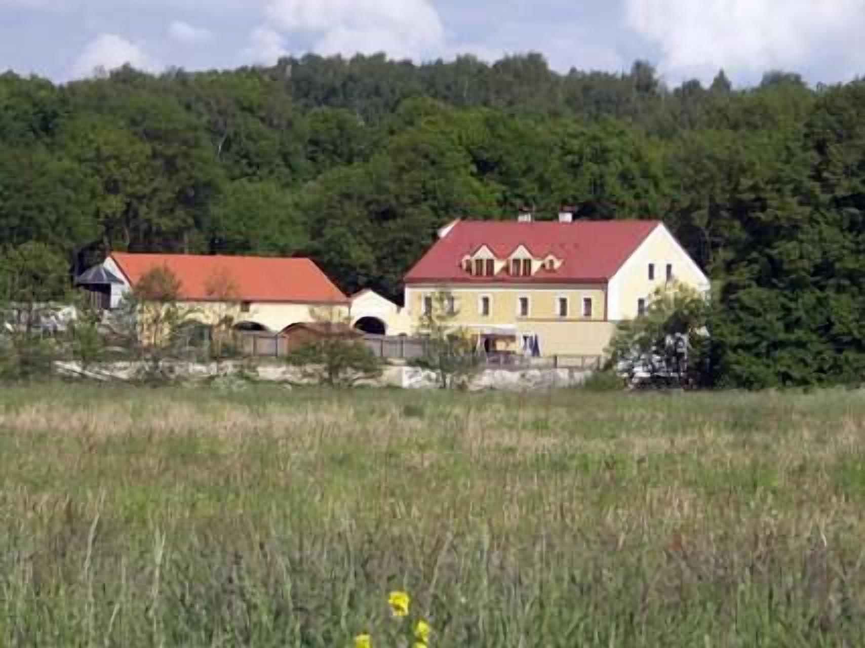 A rural house with a red roof, surrounded by a forested area.