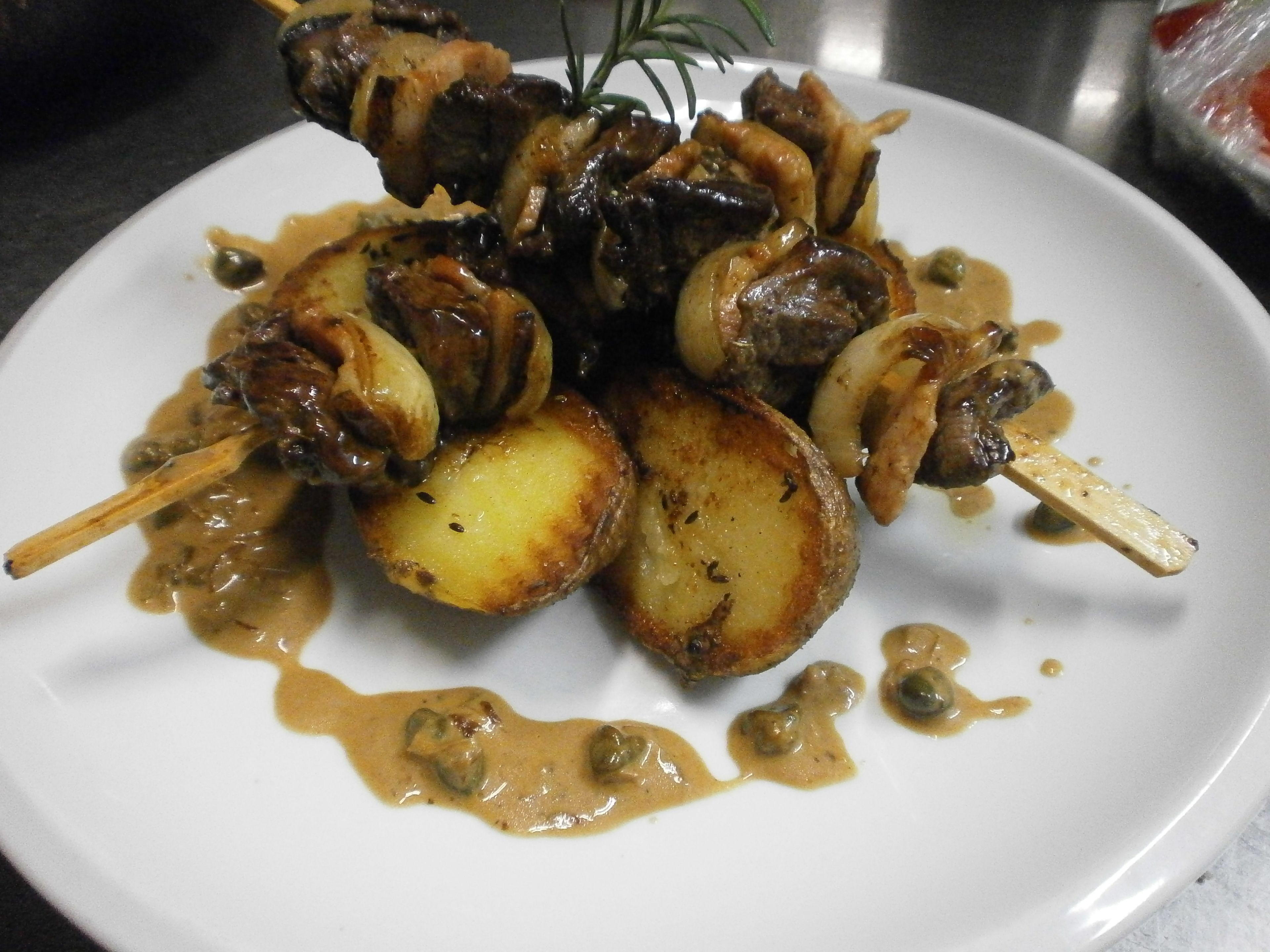 Un plato de comida con brochetas, patatas y salsa cremosa.
