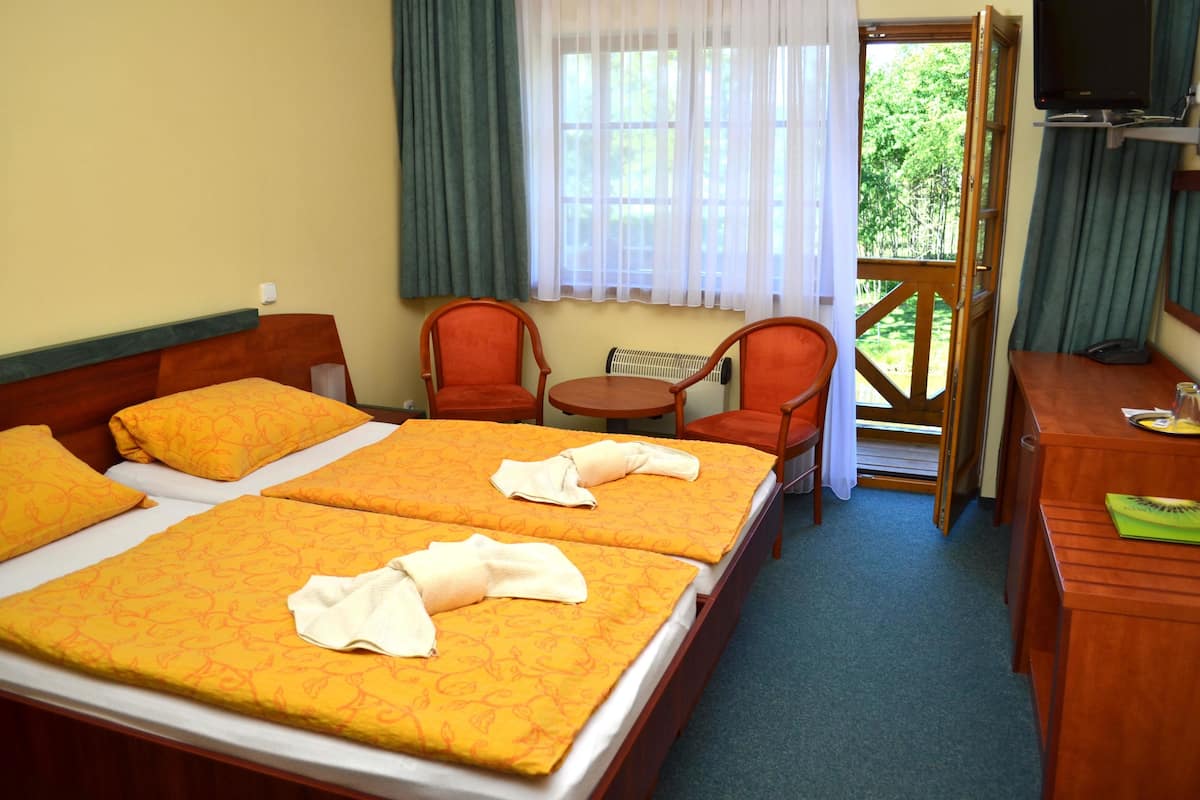 A hotel room with two beds, a desk, a chair, a small table, and a TV.