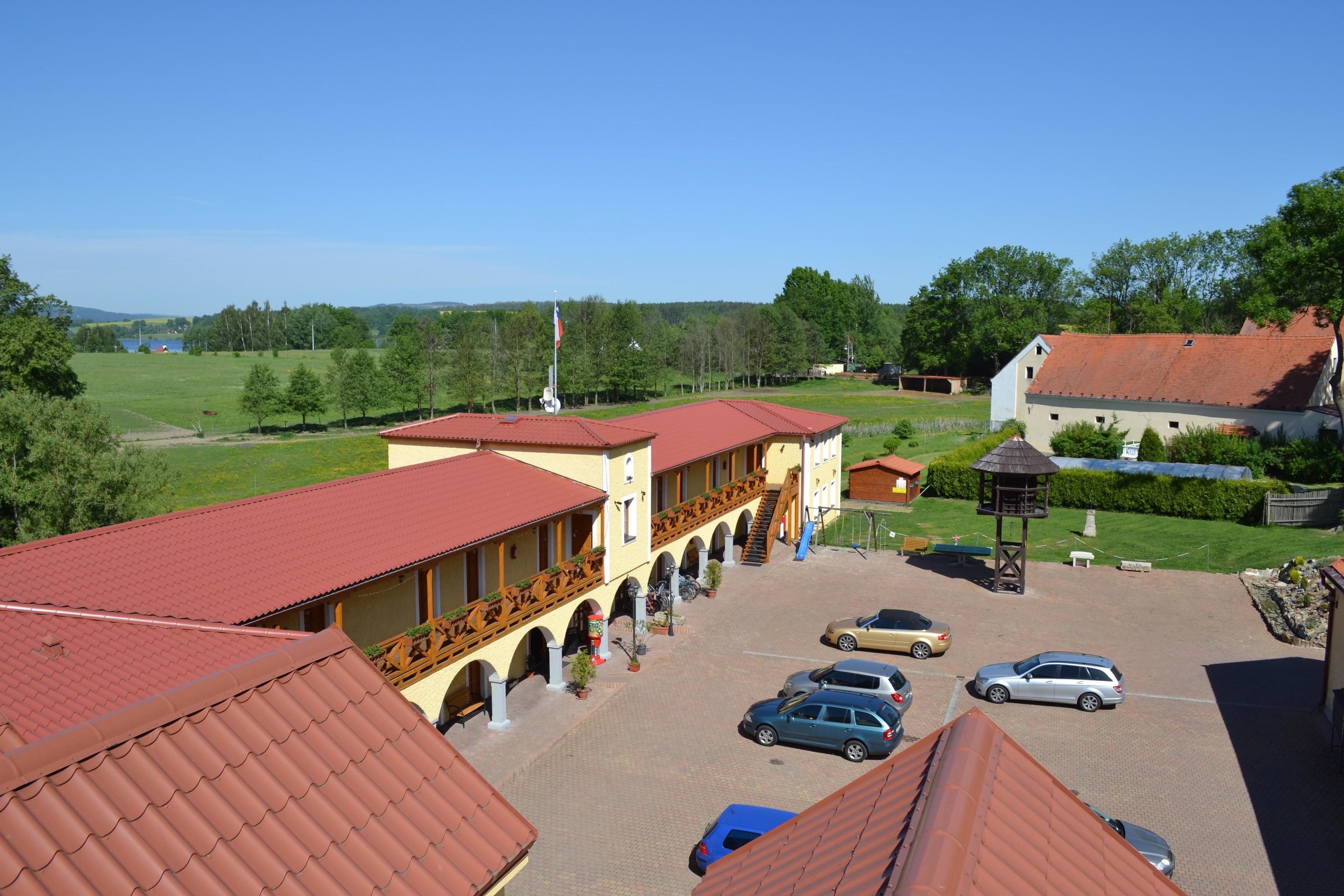 A courtyard with a building featuring a red roof, a covered walkway, and several parked cars.