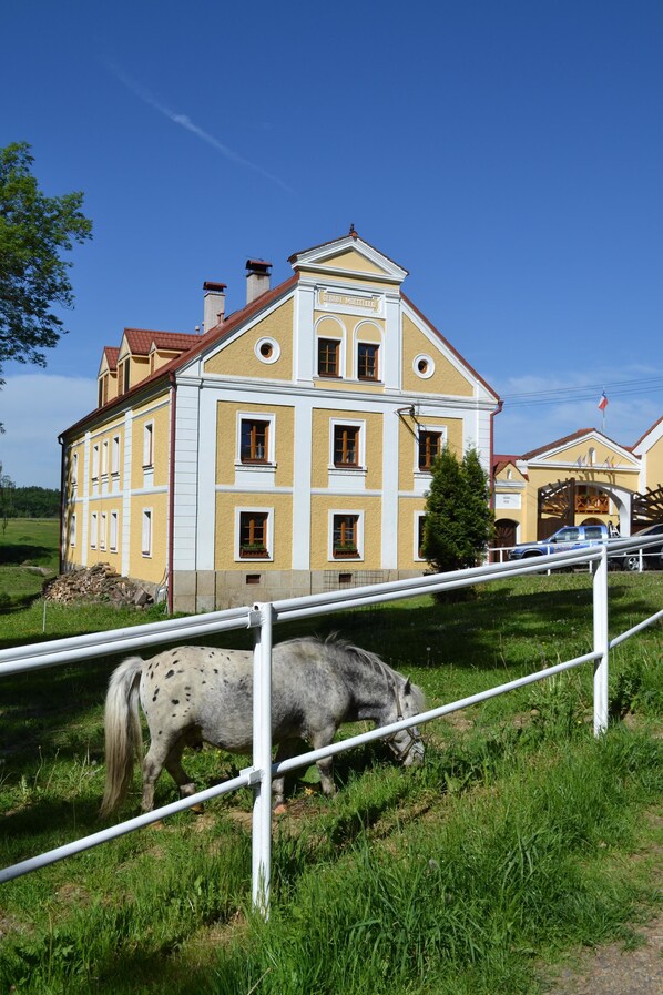 A large, yellow building with a red roof, surrounded by green grass and a white fence.