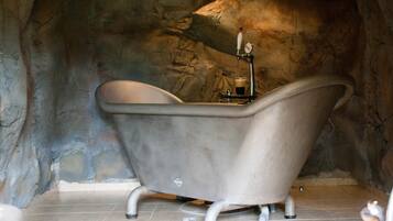Une baignoire sur pieds, de style ancien, dans une salle de bain aux murs en pierre.