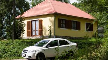 A yellow building with a red roof, a white car parked in front, and greenery around.