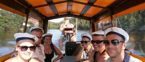 A group of people on a boat with a covered deck and a steering wheel in the center.
