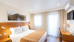 Ein Hotelzimmer mit einem großen Bett, einem Schreibtisch mit Lampe, einem Fernseher und einem Bild an der Wand.